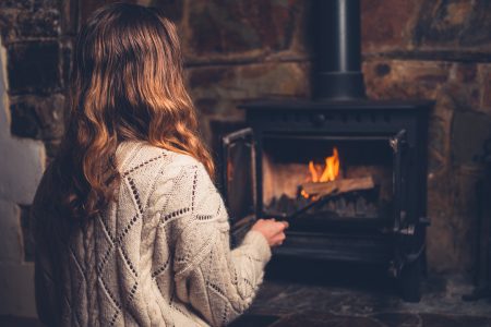 A young woman is poking a fire in a log burner